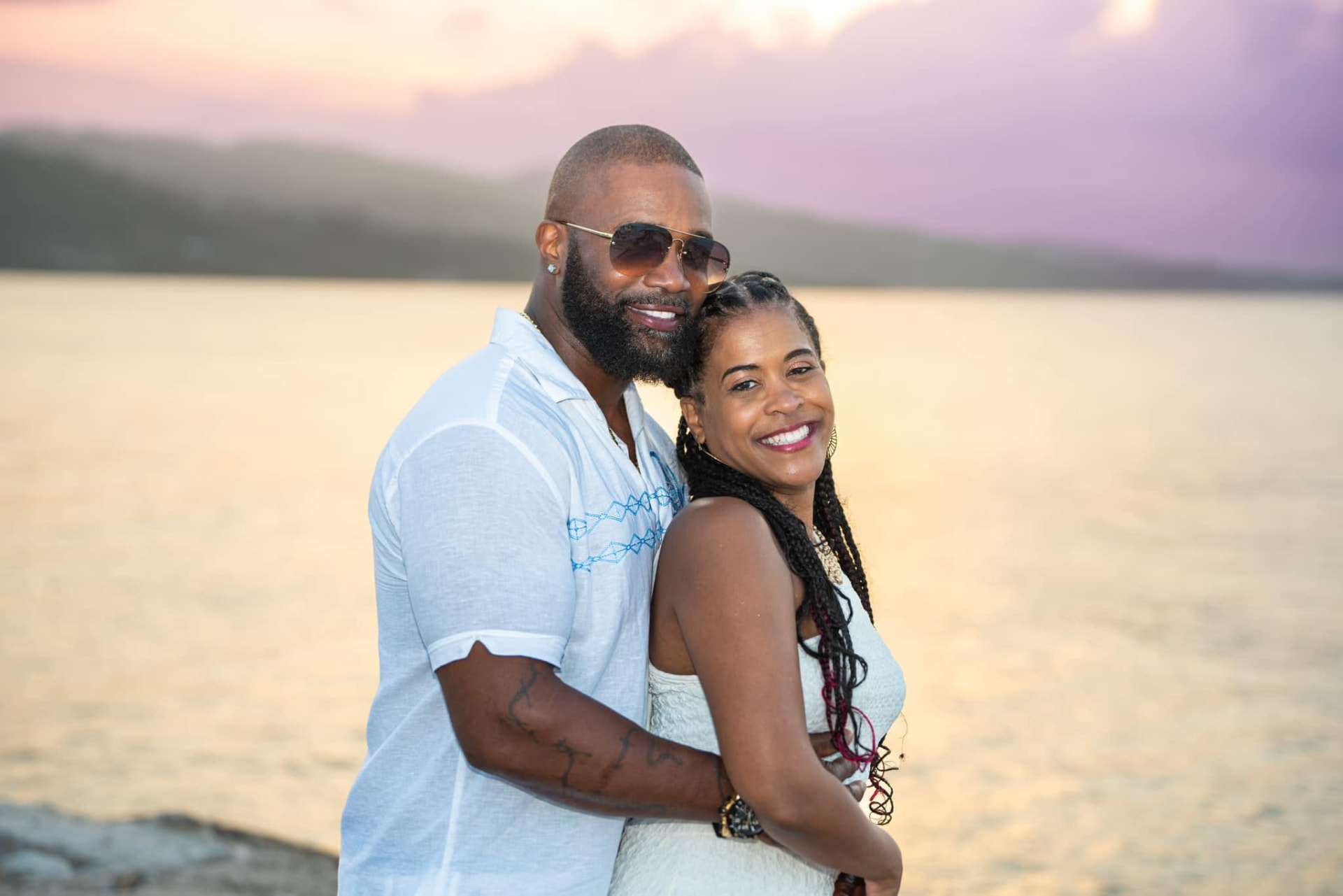 Roderick Anthony and his wife standing close together outdoors beside the water at sunset, both smiling toward the camera.